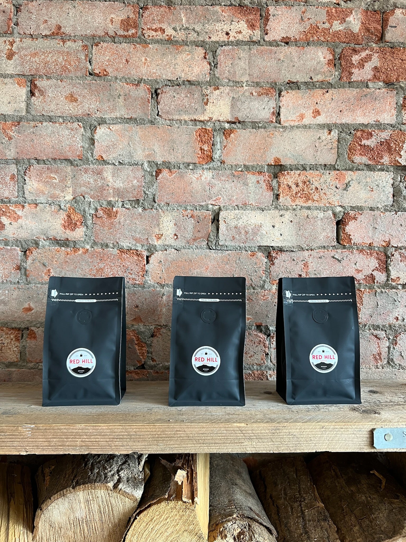 Three bags of Red Hill Coffee House Blend against the café's exposed brick wall