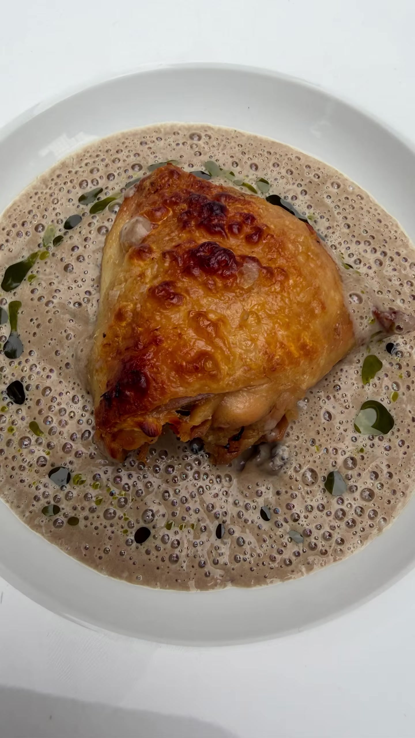 A golden main course with a foamed sauce and herb oil