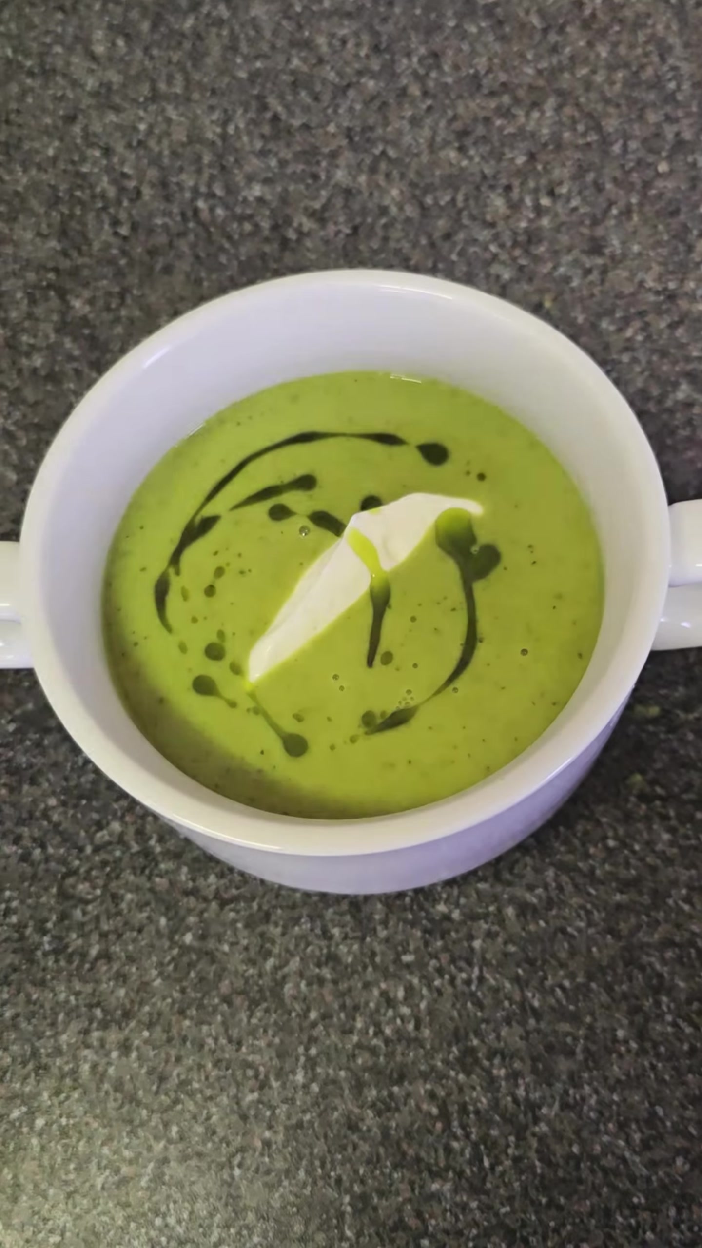 A cup of green soup finished with cream and herb oil at a previous Supper Club